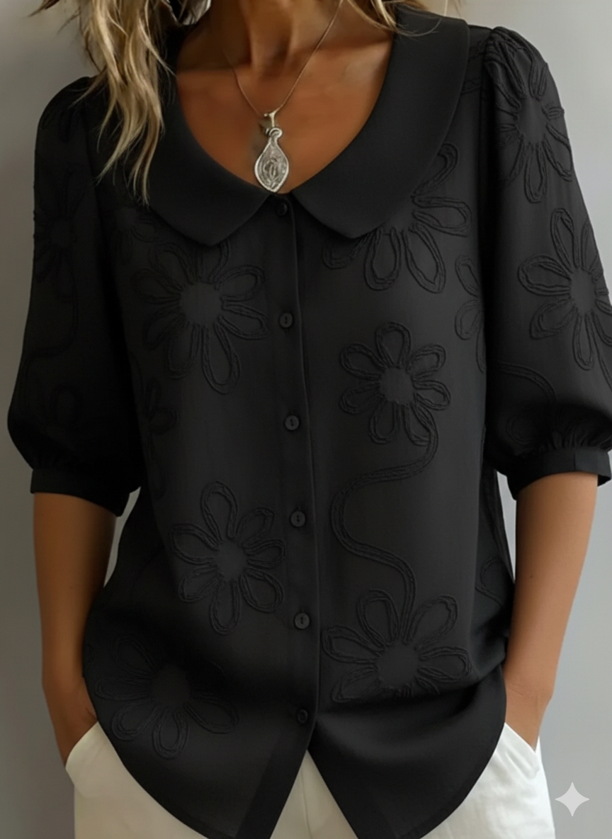 Blusa negra ligera con bordado floral, cuello solapa y botones al frente, manga tres cuartos.