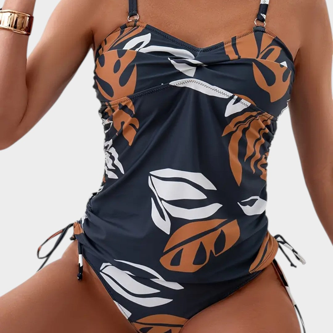 Bañador entero azul marino con estampado tropical naranja y blanco, fruncido y lazos laterales.
