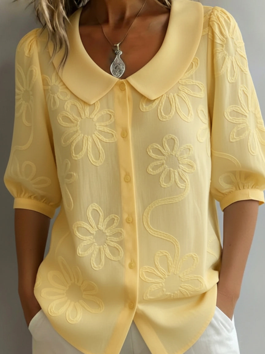 Blusa ligera amarilla con flores bordadas, cuello camisero y botones, manga tres cuartos.
