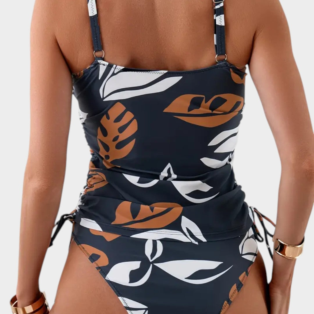 Bañador entero azul marino con estampado tropical naranja y blanco, parte trasera con tirantes.