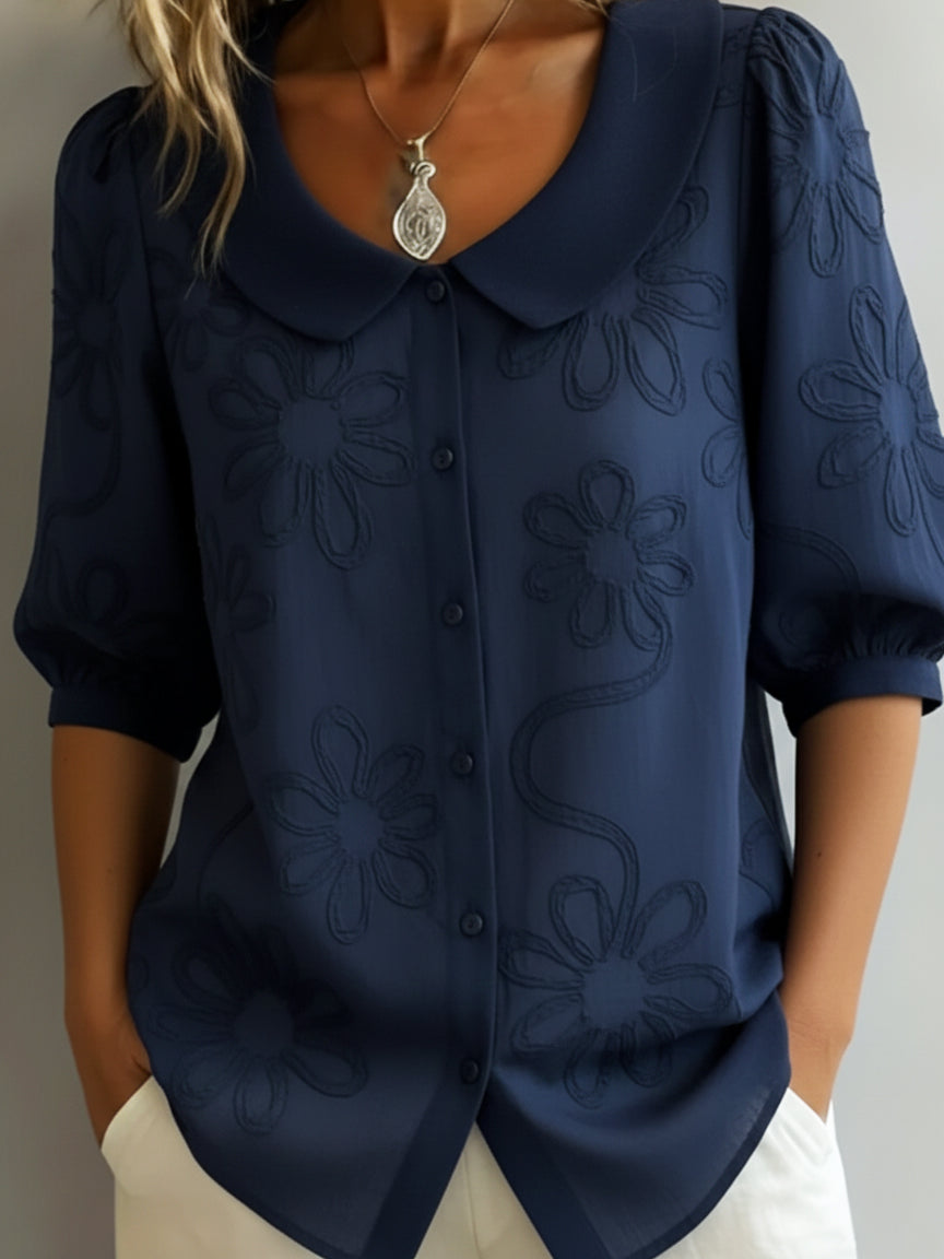 Blusa ligera azul oscuro con bordado floral, cuello solapa y botones frontales, manga tres cuartos.