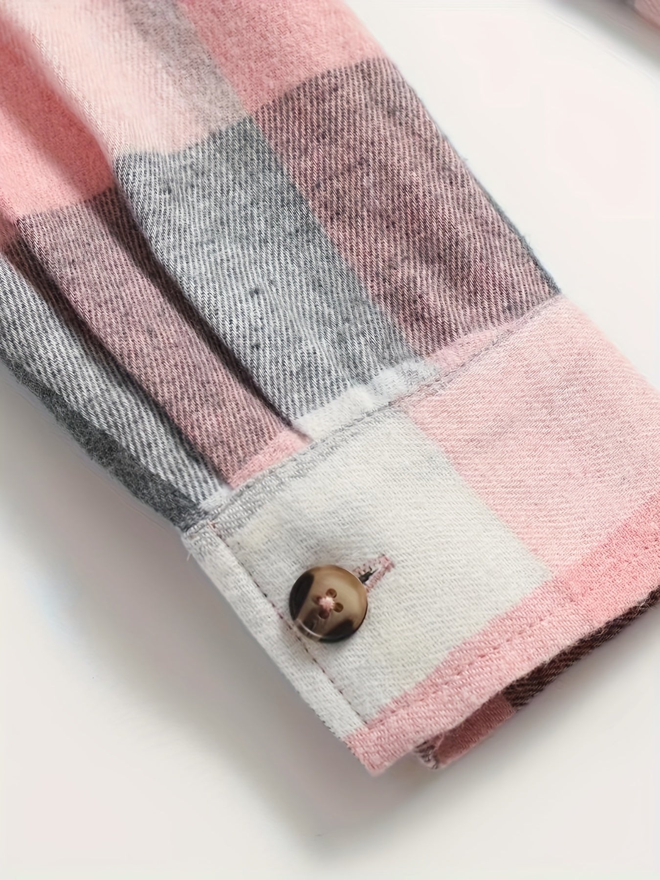 Borde y botón de camisa de cuadros rosa, gris y blanco, con dobladillo visible.