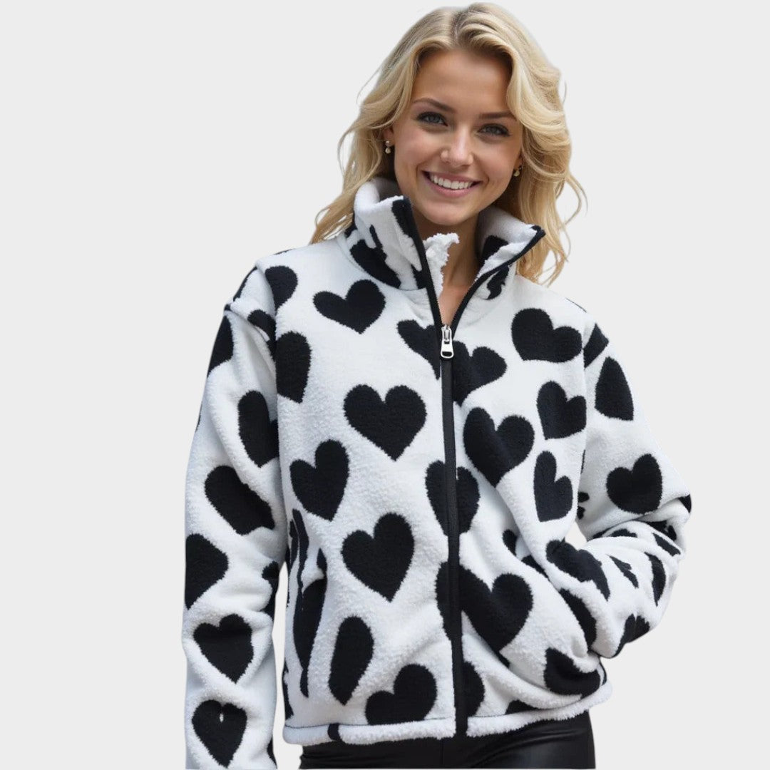 Chaqueta reversible de forro polar claro con corazones negros y cierre frontal.