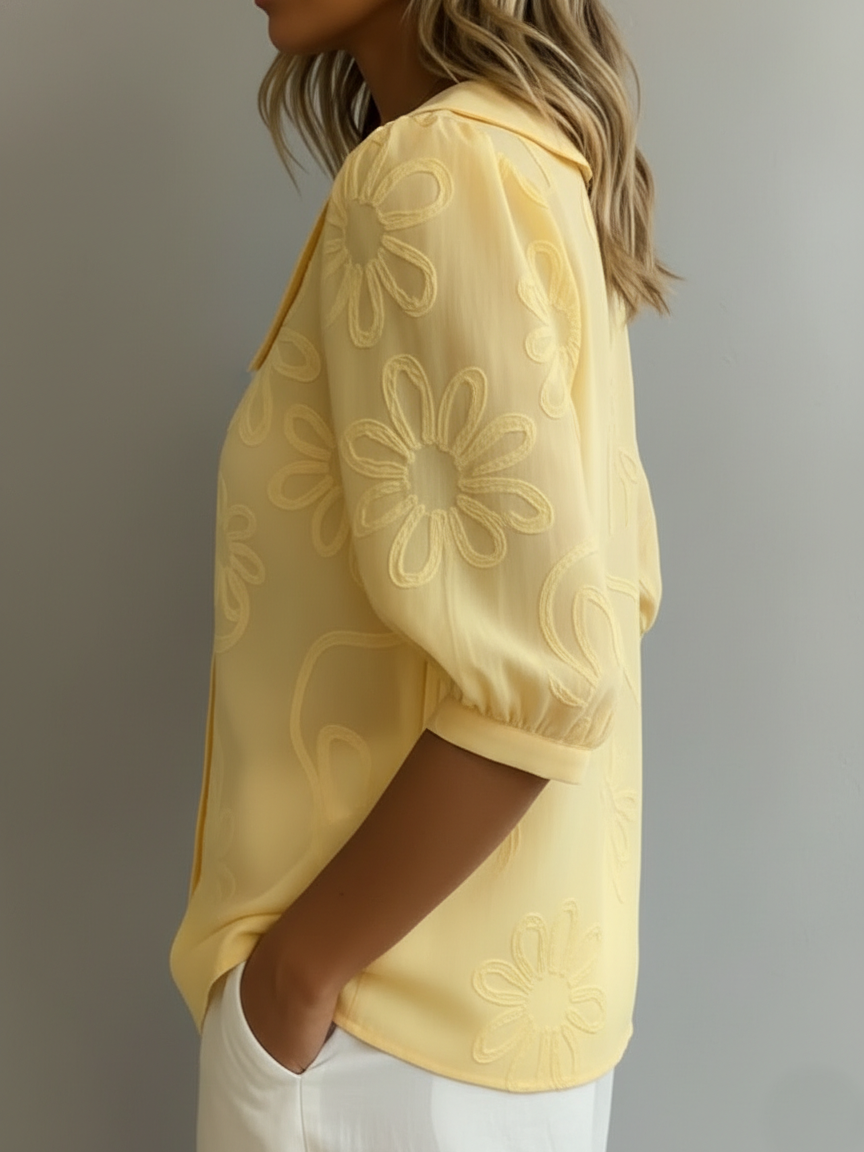 Blusa ligera amarilla con flores bordadas en relieve, manga globo y botones frontales.