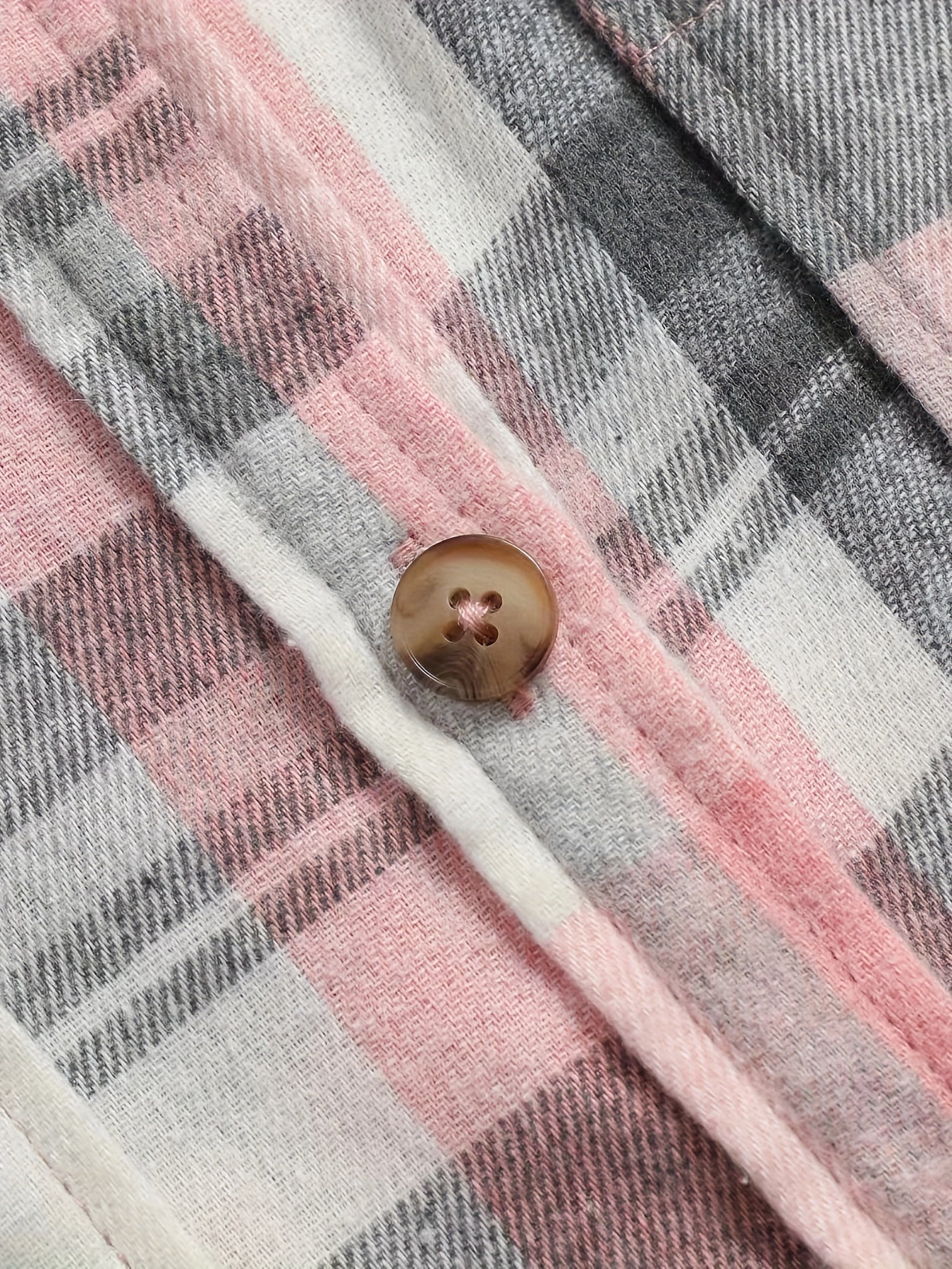 Detalle de botón marrón en camisa de cuadros rosa, gris y blanco con costuras visibles.