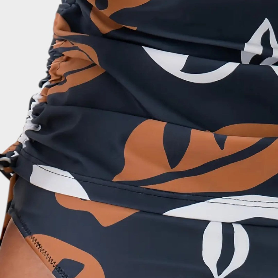 Bañador entero azul marino con estampado tropical naranja y blanco, detalle de tela fruncida.