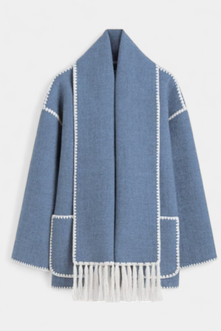 Abrigo azul con bufanda integrada y ribete blanco; flecos en el bajo.