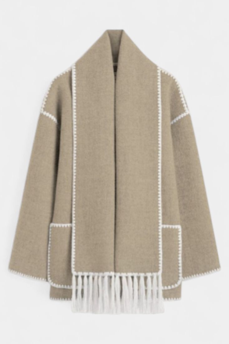 Abrigo beige claro con bufanda de flecos integrada y ribete blanco en contraste.